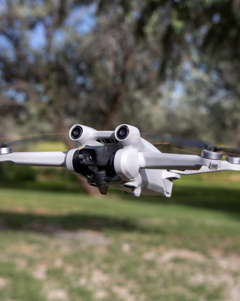 Close up drone with camera sensors and props flying in air with nature behind - DJI Mini 3 Pro aerial uav